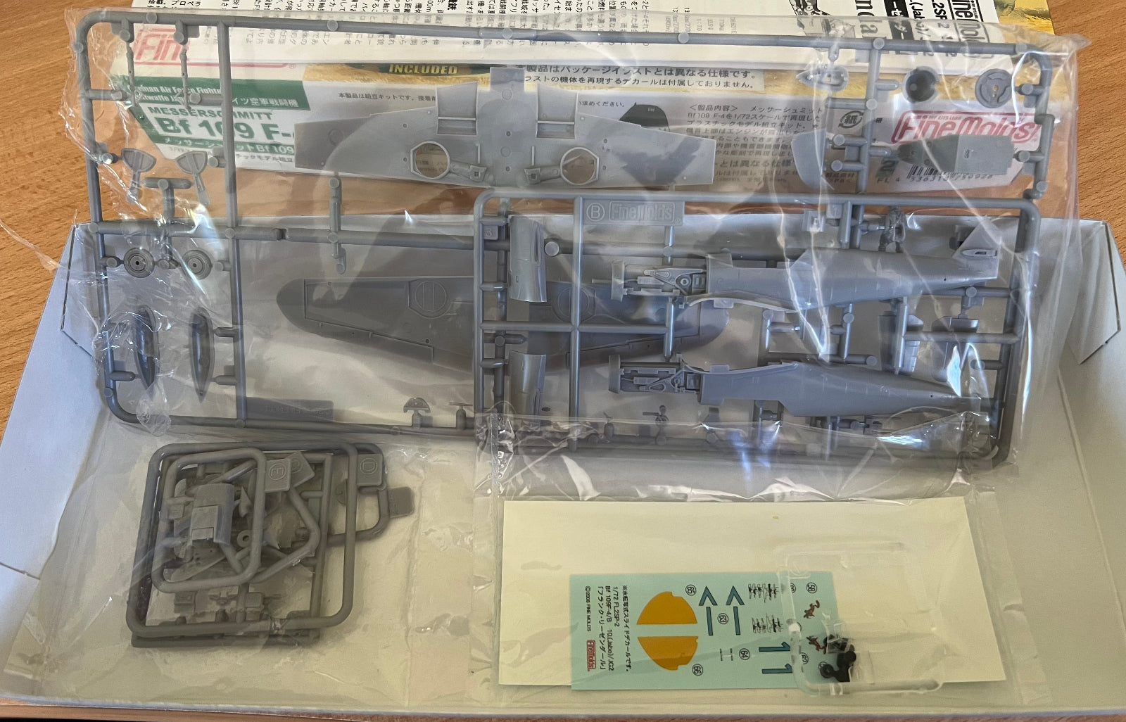 Model kit packaging with clear plastic parts and printed instructions on a wooden surface.