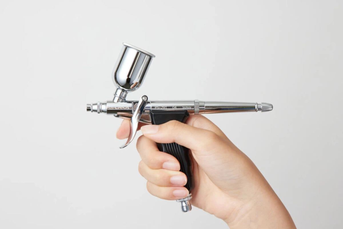 Hand holding a spray gun against a light gray background