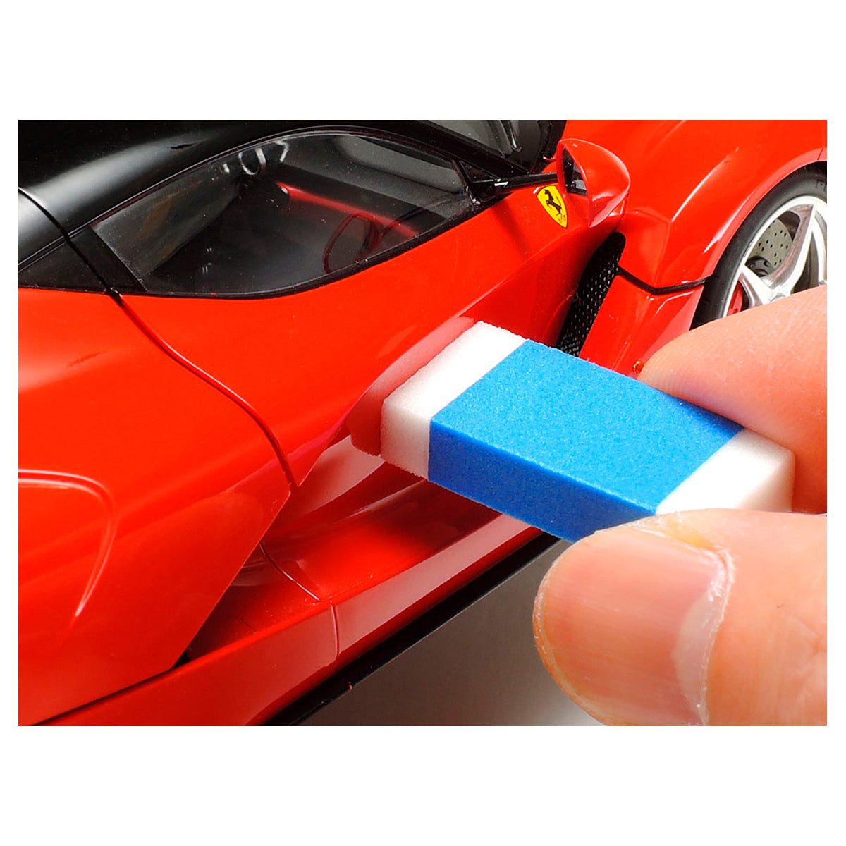 Person using a Tamiya blue and white polishing sponge to polish the side of a red model Ferrari