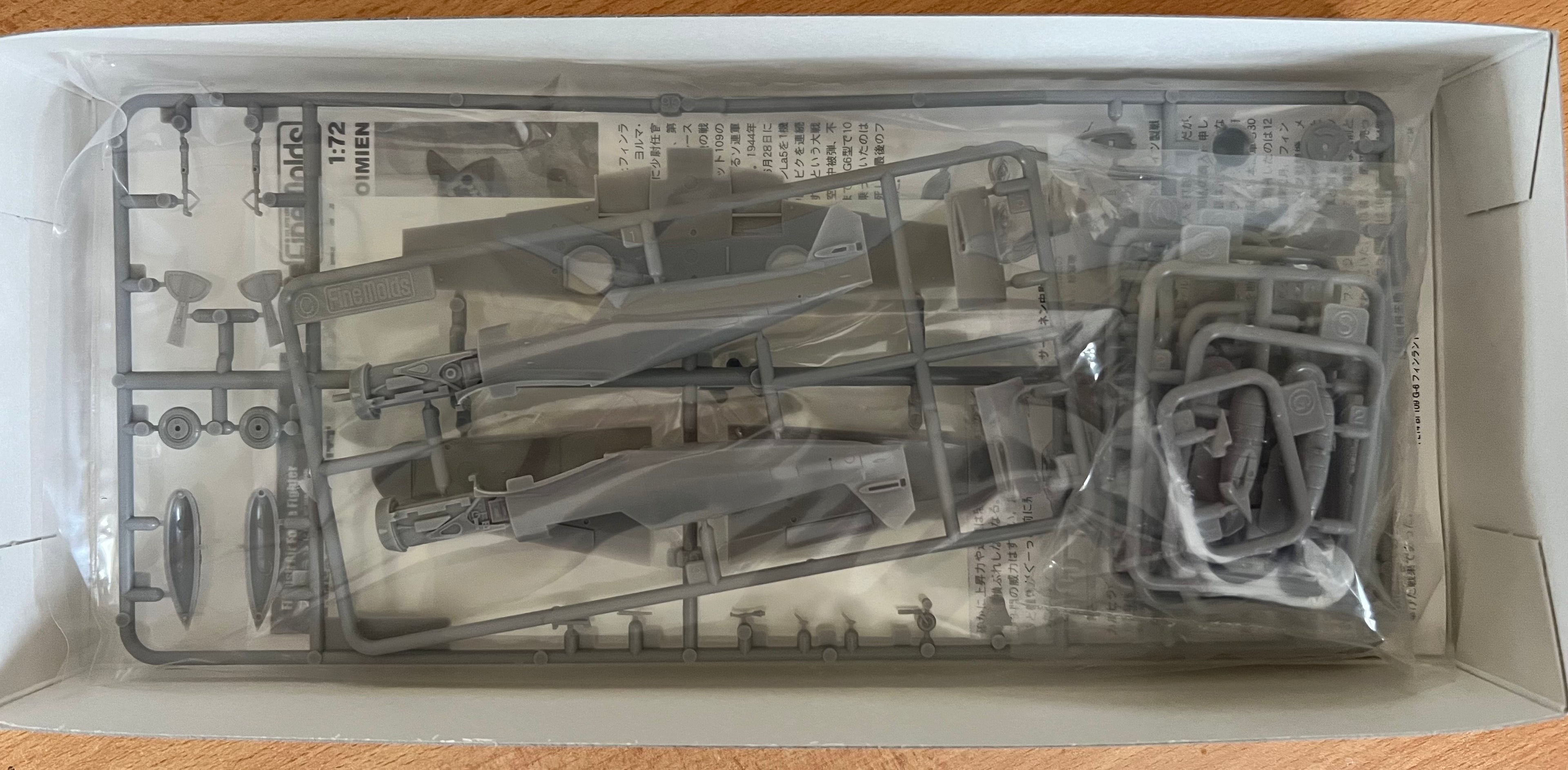 Model kit components in a clear plastic tray on a wooden surface